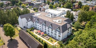 Moderne Seniorenwohnanlage mit grünem Innenhof und roten Sonnenschirmen.