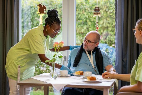 Pflegerin umsorgt Bewohner beim Kaffee und Kuchen in betreutem Wohnen.