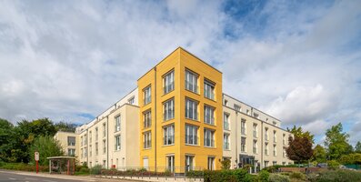 Moderne Wohnanlage mit heller Fassade und markantem gelbem Eckgebäude.