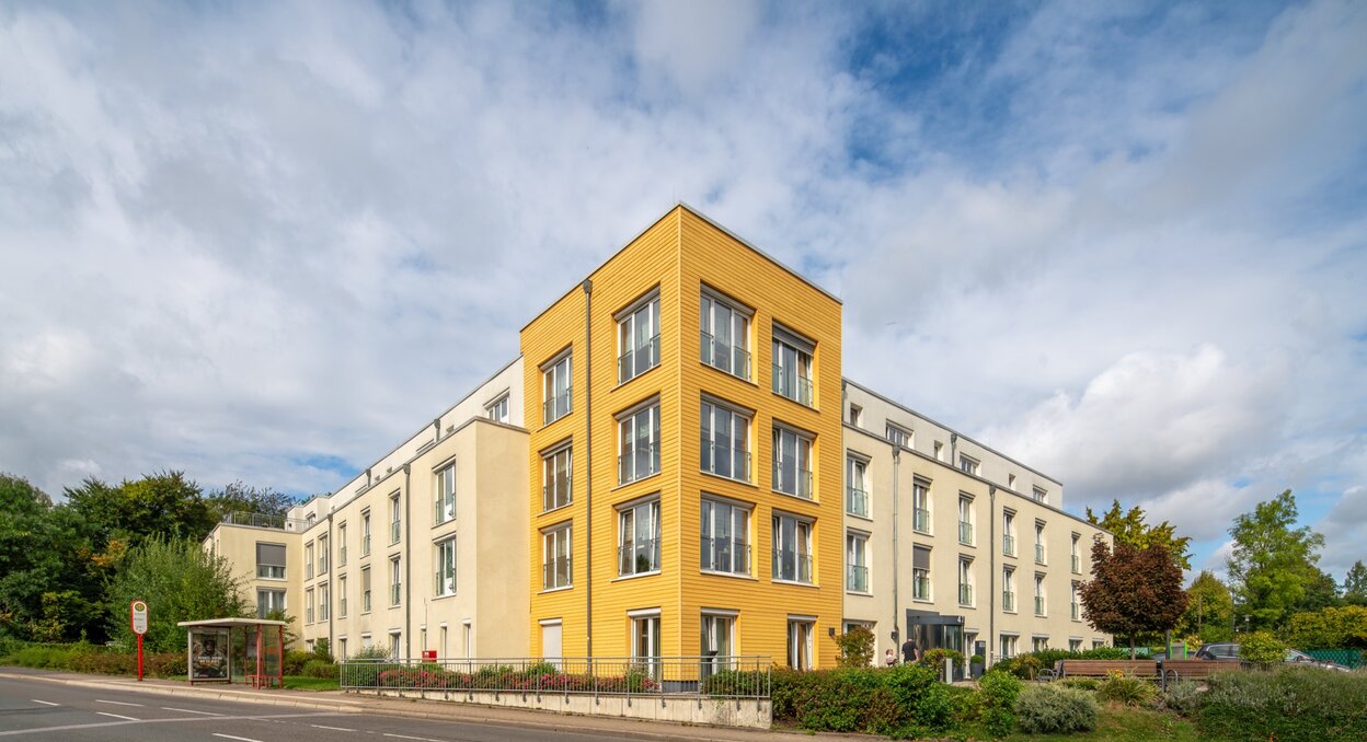 Moderne Wohnanlage mit heller Fassade und markantem gelbem Eckgebäude.