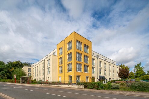 Moderne Wohnanlage mit heller Fassade und markantem gelbem Eckgebäude.