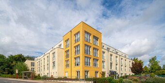 Moderne Wohnanlage mit heller Fassade und markantem gelbem Eckgebäude.