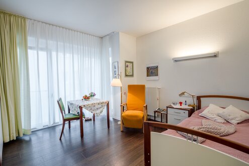 Wohnraum in einer Einrichtung: Bett, Esstisch, Sessel, viel Licht.