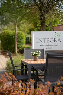 Sitzgruppe mit Blumen vor dem Schild des Integra Seniorenpflegezentrums Menden.