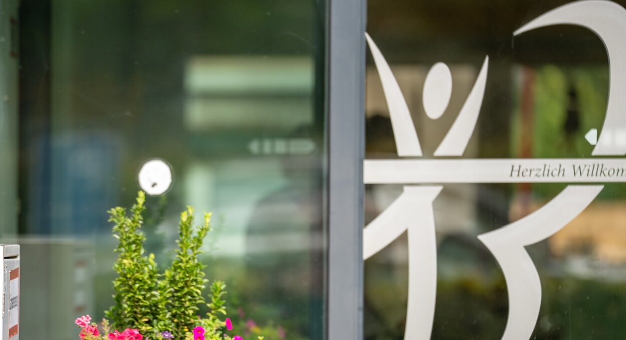 Eingangsbereich einer Wohnanlage mit Blumenkübel und Willkommensgruß auf Glastür.