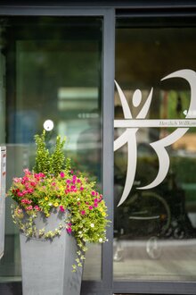 Eingangsbereich einer Wohnanlage mit Blumenkübel und Willkommensgruß auf Glastür.