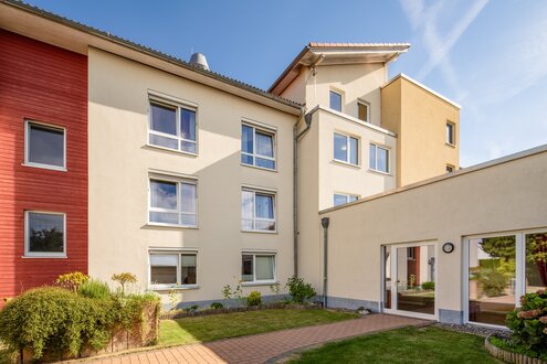 Modernes Gebäude einer betreuten Wohnanlage mit Garten und blauem Himmel.