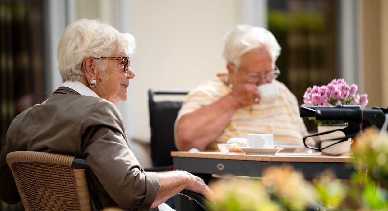 Zwei Seniorinnen sitzen im Freien an einem Tisch und trinken Kaffee.