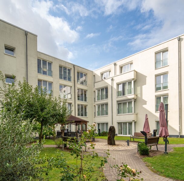 Innenhof einer Senioren-Wohnanlage mit grünem Garten, Wegen, Bänken und Pavillon.