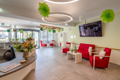 Heller Empfangsbereich einer Wohnanlage mit Rezeption und roten Sitzgruppen.