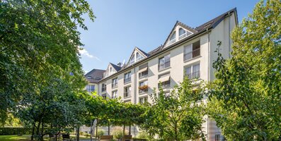 Mehrstöckiges Wohngebäude mit Balkonen, umgeben von gepflegtem Grün und Sitzbänken.