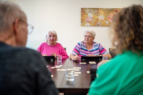 Vier ältere Menschen spielen gemeinsam ein Tischspiel in einer Wohnanlage.