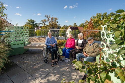 Vier Senioren genießen den sonnigen Tag auf der Dachterrasse einer Wohnanlage.