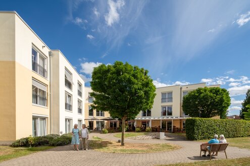 Betreutes Wohnen: Moderne Gebäude mit sonnigem Innenhof und Senioren im Freien.