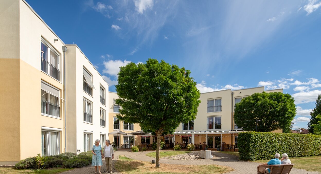 Betreutes Wohnen: Moderne Gebäude mit sonnigem Innenhof und Senioren im Freien.