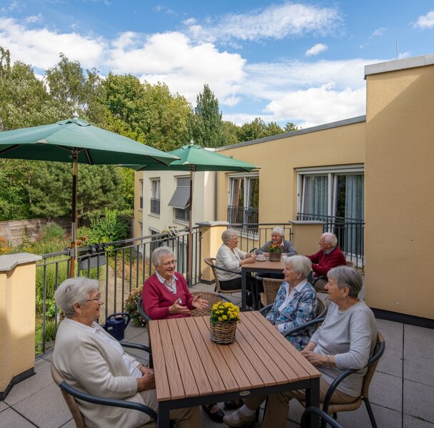 Senioren sitzen auf der Terrasse einer Wohnanlage und unterhalten sich.