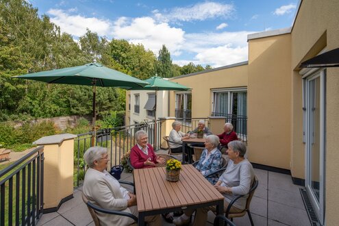 Senioren sitzen auf der Terrasse einer Wohnanlage und unterhalten sich.