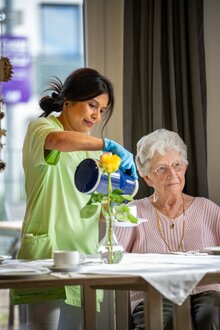 Pflegekraft gießt Seniorin in einer Wohnanlage ein Getränk ein.