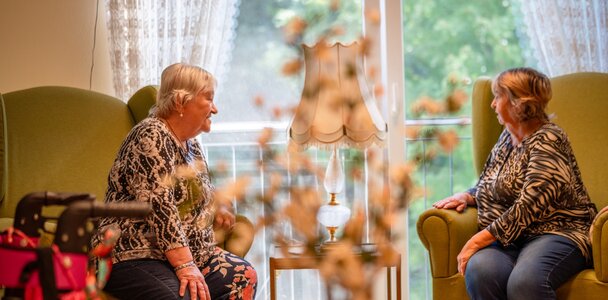 Lachende Seniorinnen unterhalten sich in bequemen Sesseln einer Einrichtung.