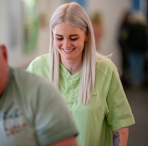 Lächelnde Betreuungskraft in grüner Uniform schiebt Gehhilfe.