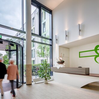 Helle Rezeption einer modernen Wohnanlage für betreutes Wohnen mit Drehtür und grünem Logo.