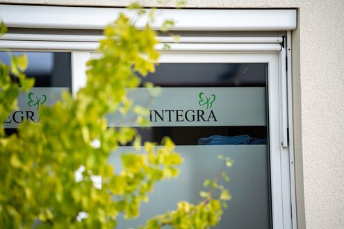 INTEGRA Logo und Schriftzug an einem Fenster einer betreuten Wohnanlage, unscharfe Blätter im Vordergrund.