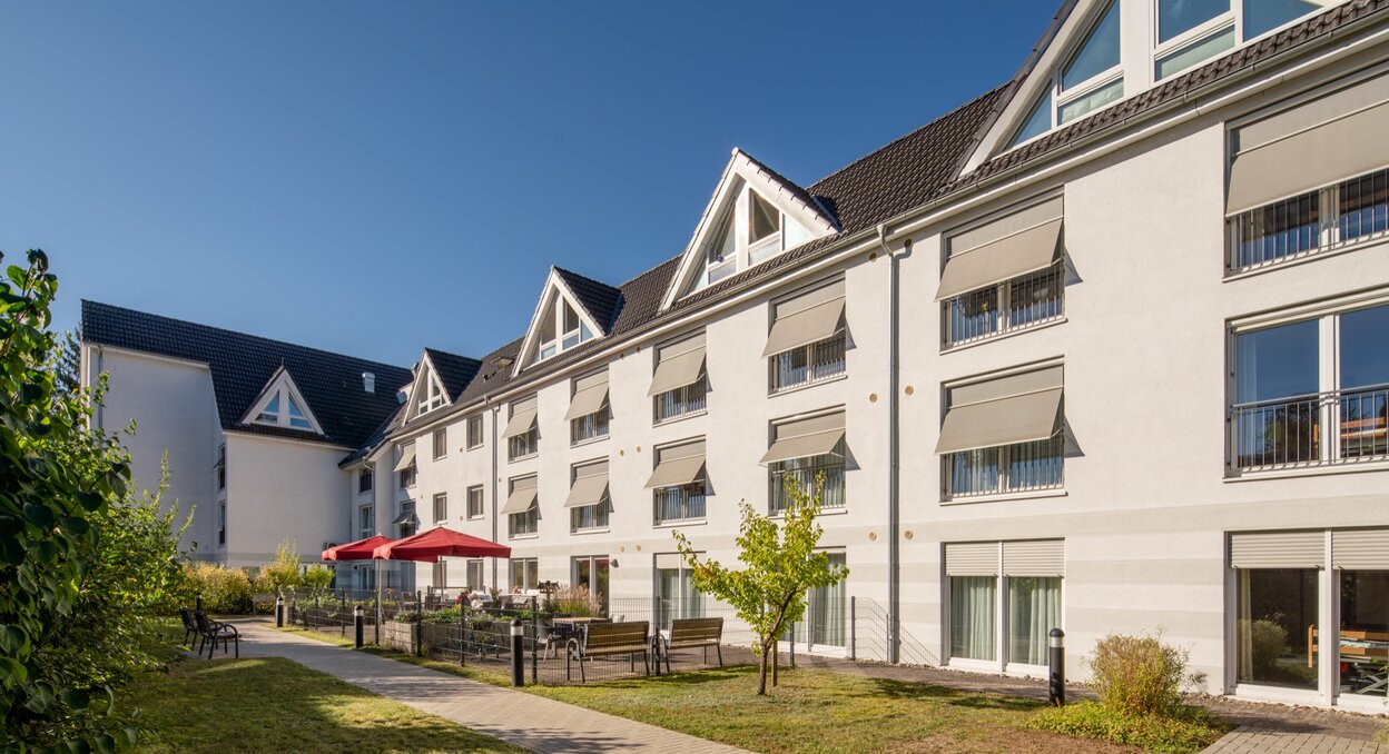 Moderne Einrichtung für betreutes Wohnen mit heller Fassade, Grünflächen und Außenterrasse.