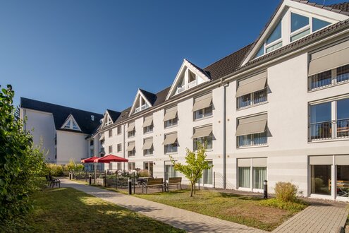Moderne Einrichtung für betreutes Wohnen mit heller Fassade, Grünflächen und Außenterrasse.