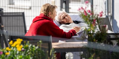Frau hält Hand einer liegenden Seniorin im Freien.