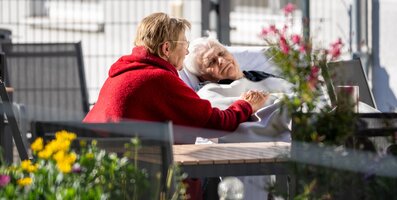 Frau hält Hand einer liegenden Seniorin im Freien.