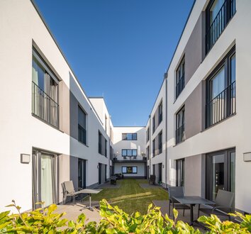 Innenhof einer modernen Wohnanlage mit Grünfläche, Terrassen und Sitzgelegenheiten.