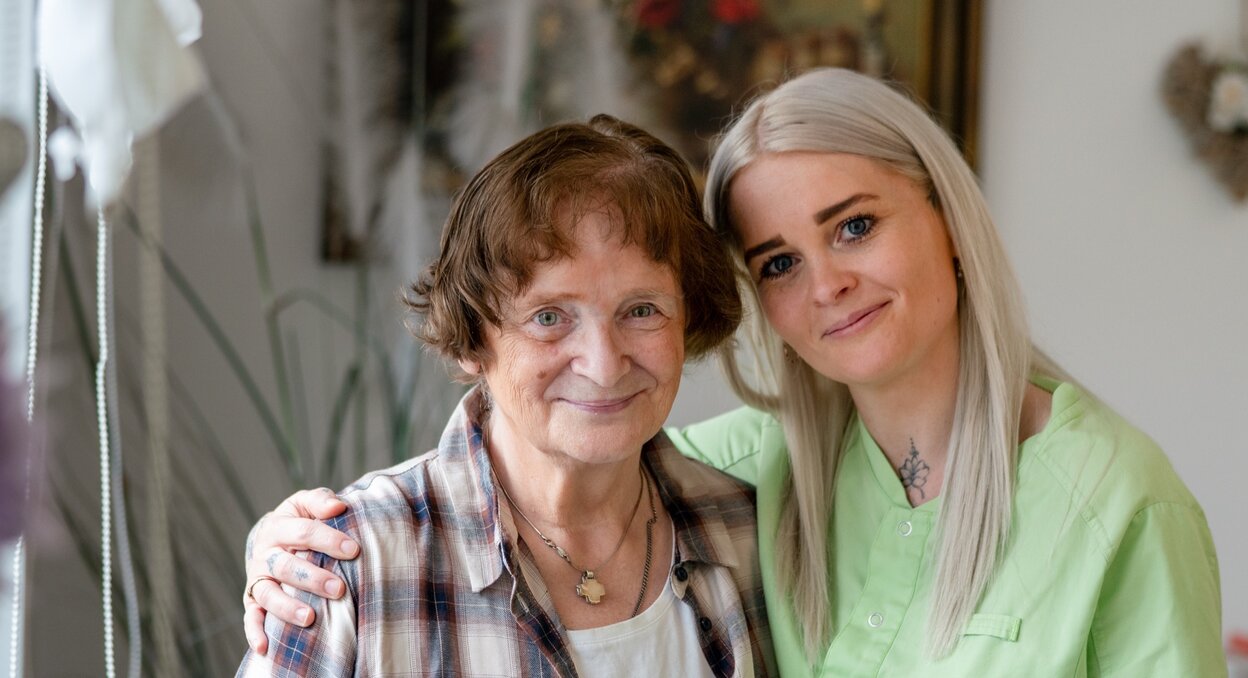 Lächelnde Seniorin und Pflegerin in einer Wohnanlage.