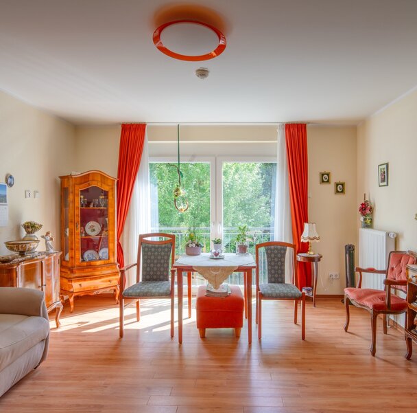 Helles Wohnzimmer mit Esstisch, Stühlen, Sessel und traditionellen Möbeln in einer Wohnanlage.