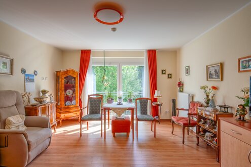 Helles Wohnzimmer mit Esstisch, Stühlen, Sessel und traditionellen Möbeln in einer Wohnanlage.