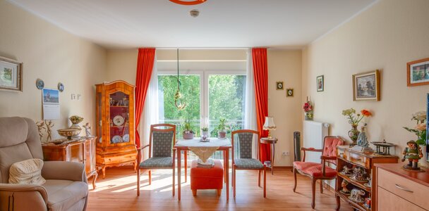 Helles Wohnzimmer mit Esstisch, Stühlen, Sessel und traditionellen Möbeln in einer Wohnanlage.