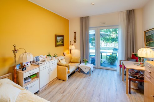 Helles, möbliertes Wohnzimmer mit Schlafbereich und Balkontür in einer Wohnanlage.