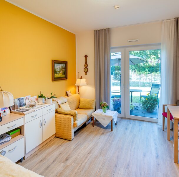 Helles, möbliertes Wohnzimmer mit Schlafbereich und Balkontür in einer Wohnanlage.