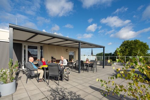 Senioren sitzen auf einer sonnigen Terrasse einer betreuten Wohnanlage.