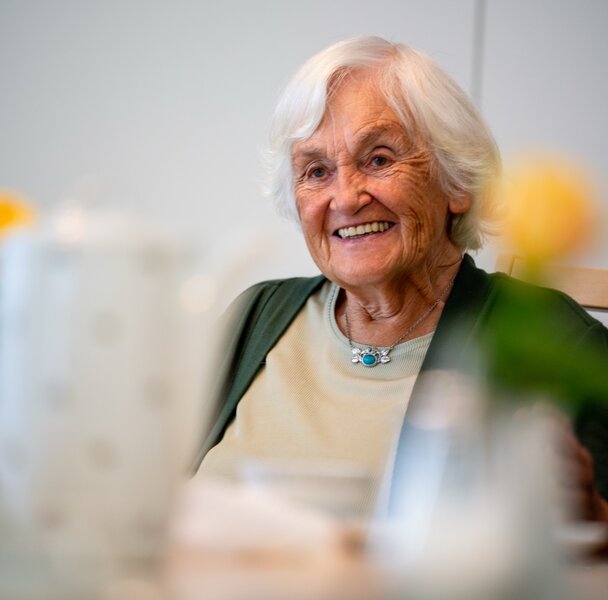 Fröhliche Seniorin mit weißen Haaren lächelt in einer Einrichtung für betreutes Wohnen.