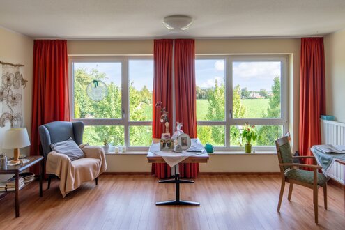 Gemütlicher Wohnraum mit großer Fensterfront und Blick ins Grüne in einer Seniorenwohnanlage.